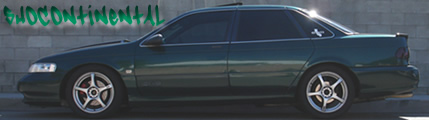 1993 Ford Taurus - Side view of a dark green sedan parked against a brick wall with graffiti.