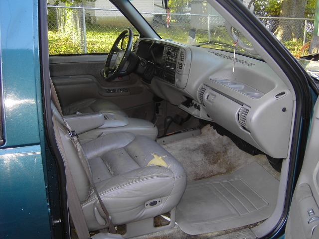 Worn gray leather front seat and dashboard seen through the open passenger door of a teal GM truck