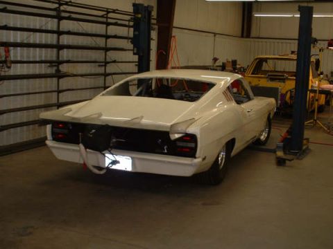 2005 Ford Mustang - A white coupe, likely a 1969 model, is shown in a workshop with racing modifications. A yellow vehicle is visible in the background.