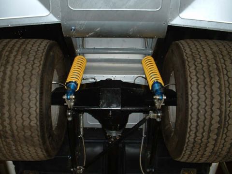 2005 Ford Mustang - The rear suspension and axle assembly of a vehicle are visible, large tires and bright yellow shock absorbers.