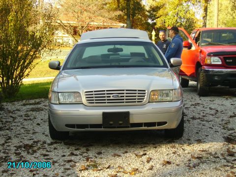 2002 Ford Crown Victoria - A silver 2002 Ford Crown Victoria is parked in a gravel driveway next to a red pickup truck.