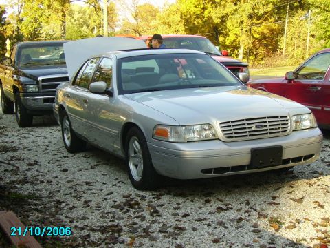 2002 Ford Crown Victoria - A silver 2002 Ford Crown Victoria is parked outside with its hood up, alongside other vehicles.