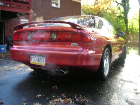 1995 Ford Probe - A red 1995 Ford Probe is parked outside a brick building, with steam rising from its rear.