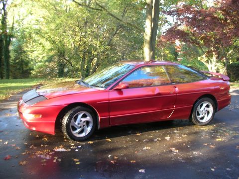 1995 Ford Probe - A red 1995 Ford Probe is seen from the side, parked on a wet driveway with fallen leaves.
