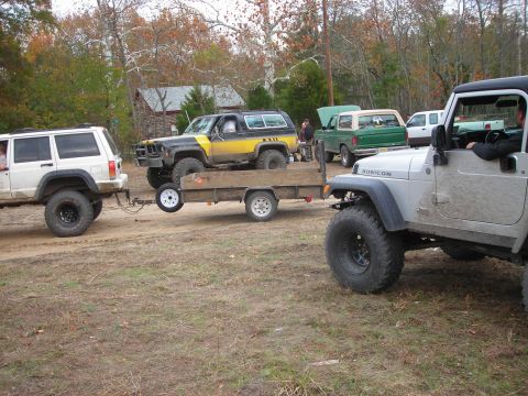 1997 Jeep TJ - Several off-road vehicles are gathered in a dirt lot with trees in the background.