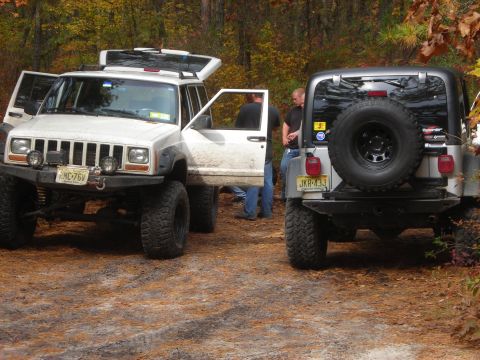 1997 Jeep TJ - Two Jeeps are parked on a dirt road surrounded by trees in the fall.