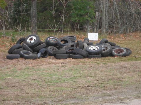 1997 Jeep TJ - A large collection of discarded tires is piled haphazardly on a patch of dry grass, with a sign in the background.