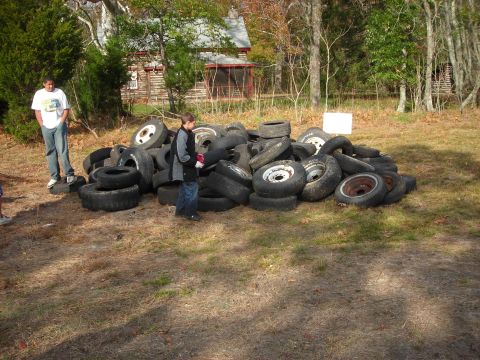 1997 Jeep TJ - A large collection of tires is piled up outdoors, with two people observing the scene near a rustic cabin.