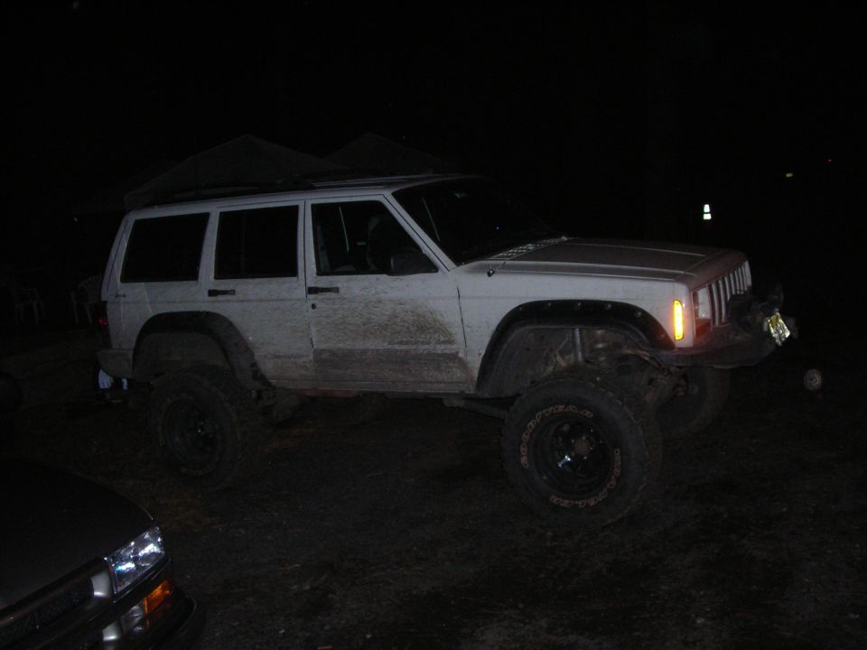 White Jeep Cherokee XJ with lifted suspension and off-road tires, parked at night