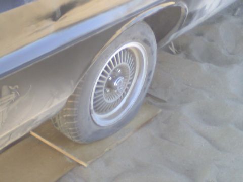 1972 Ford Ranchero - Rear wheel of a 1972 Ford Ranchero resting on planks in a sandy area.