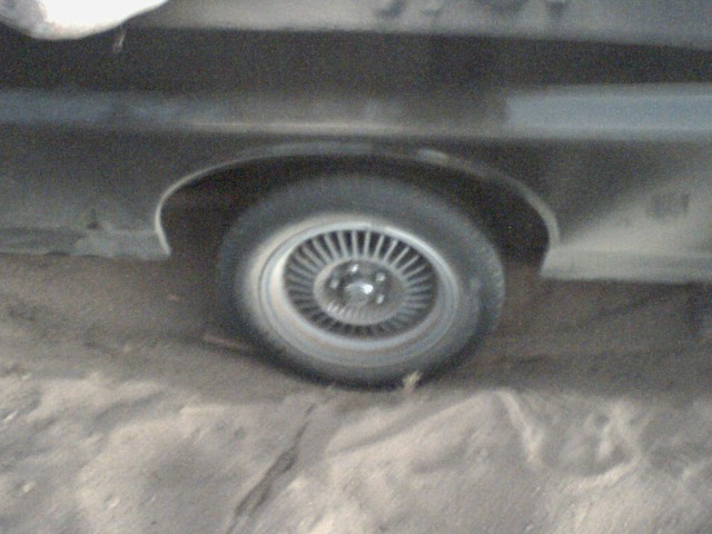 Close-up of a car's rear wheel and fender area. The wheel has a multi-spoke design