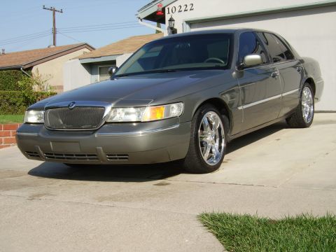 2000 Mercury Grand Marquis - A gray 2000 Mercury Grand Marquis is parked in a driveway, its chrome wheels and distinctive grille.