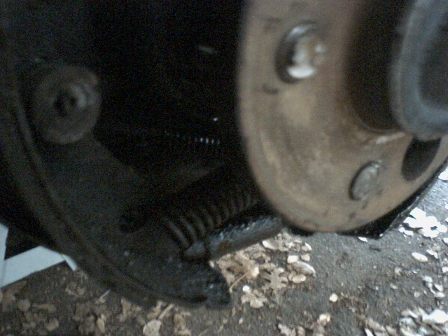 close-up of a car's brake drum and shoe assembly, showing a spring and some dirt