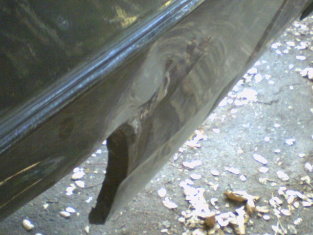 Close-up of a dented and torn dark-colored vehicle body panel near the ground