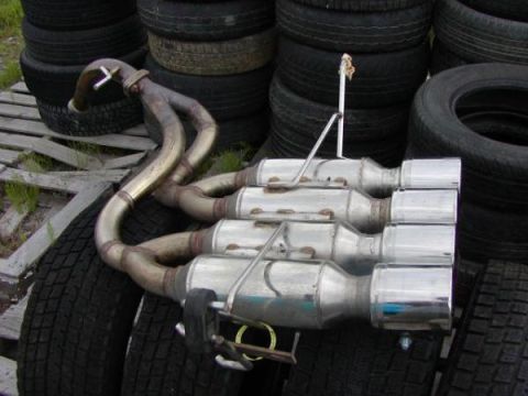 1993 Ford Taurus - Quad exhaust system with chrome tips, likely for a performance vehicle, displayed against a backdrop of tires.
