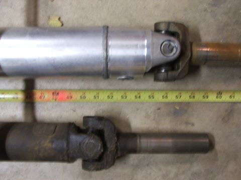 1965 Ford Mustang - A comparison of two driveshafts, one aluminum and one dark metal, with a tape measure indicating their lengths.