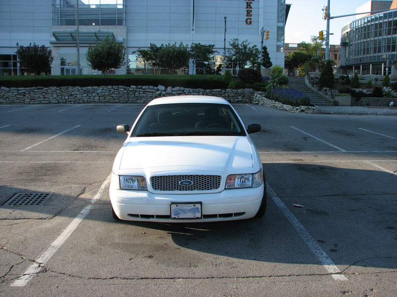 White Ford Crown Victoria front view with mesh grille and pillar spotlight in a city lot
