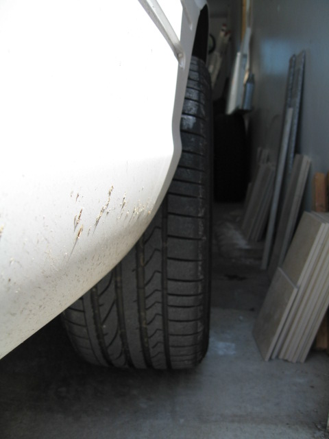 2003 Ford Crown Victoria - Close-up view of a white car's fender and tire, parked indoors.