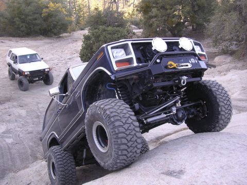 1985 Toyota 4Runner - A heavily modified dark blue SUV navigates a rocky trail, with a white SUV following behind.