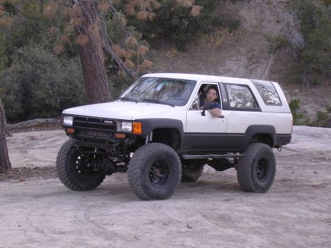 1985 Toyota 4Runner - Modified 1985 Toyota 4Runner on a dirt trail with trees and rocks in the background.