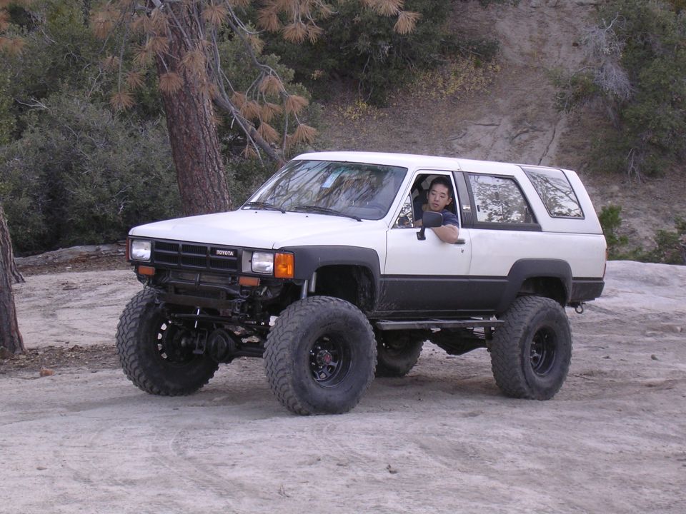 White 1985 Toyota 4Runner with large off-road tires and lift kit parked on dirt road