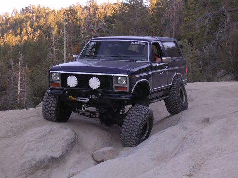 1985 Toyota 4Runner - A modified 1984 Ford Bronco II tackles a challenging rocky trail in a wooded area.