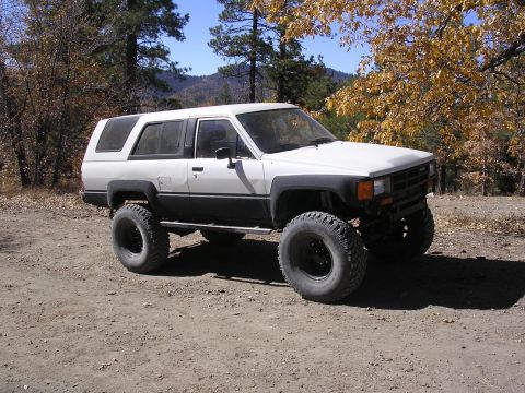 1985 Toyota 4Runner - Modified 1985 Toyota 4Runner on a dirt road with autumn foliage in the background.