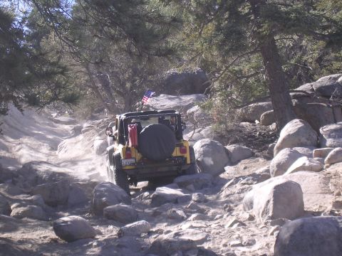 1985 Toyota 4Runner - A yellow Jeep Wrangler navigates a challenging, rocky terrain under a clear sky.