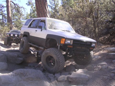 1985 Toyota 4Runner - A white 1985 Toyota 4Runner navigates a challenging rocky trail with another vehicle in the background.