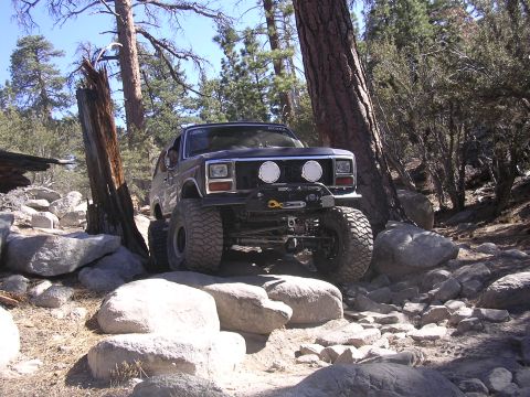 1985 Toyota 4Runner - This dark SUV, likely a Ford Bronco from the early 1980s, tackles a challenging rocky trail with its off-road tires and winch.