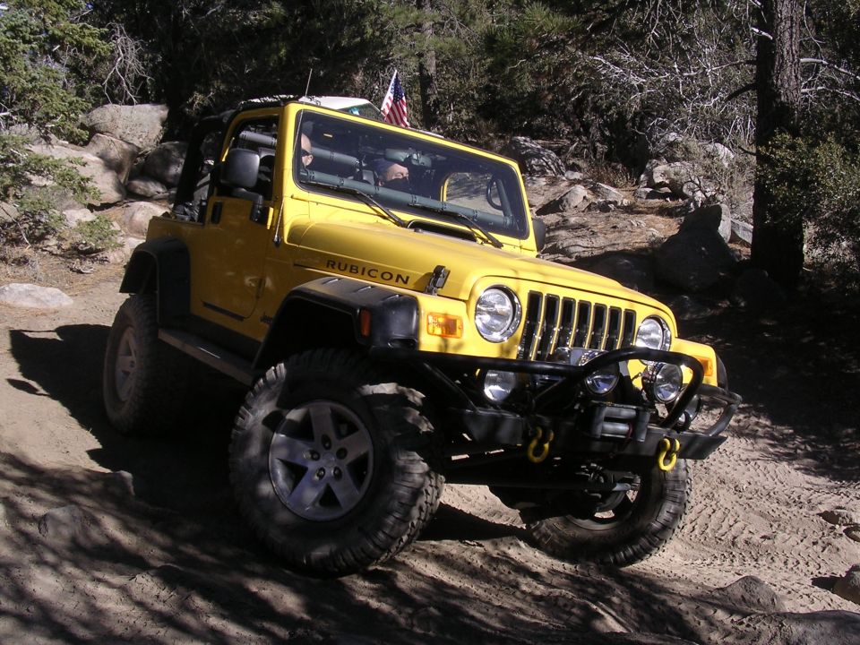 Yellow Jeep Wrangler Rubicon with "RUBICON" decal on fender, driving on dirt trail