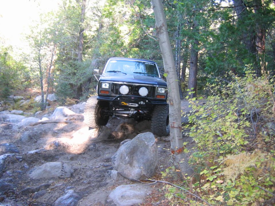 Black lifted Ford Bronco crawling over rocks on forest trail, front view with winch bumper