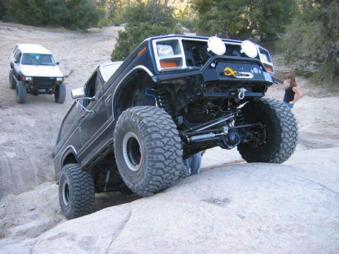 1985 Ford Bronco - This heavily modified SUV is navigating a rocky trail with another vehicle following behind.