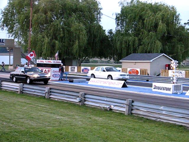 Two 2003 Ford Crown Victorias at a drag strip, one black, one white, viewed from the front
