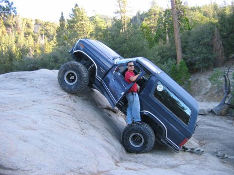 1985 Ford Bronco - This 1985 Ford Bronco is shown off-roading, climbing a large rock formation with its driver's door open.