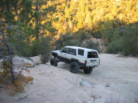 1985 Ford Bronco - A modified Toyota 4Runner navigates a challenging off-road path in a wooded, mountainous area.