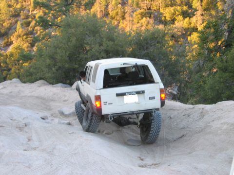 1985 Ford Bronco - A white Toyota SUV navigates a rocky, off-road trail with trees in the background.