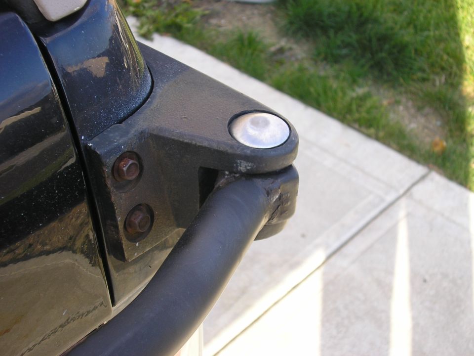 Close-up of black hinge with pivot pin and two rusted bolts on a dark vehicle panel