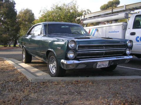 1975 Ford Ranchero - A green coupe with a distinctive chrome grille is parked beside a utility truck.