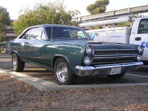 1975 Ford Ranchero - This green coupe, likely a 1966 model, is parked in a lot next to a white utility truck.