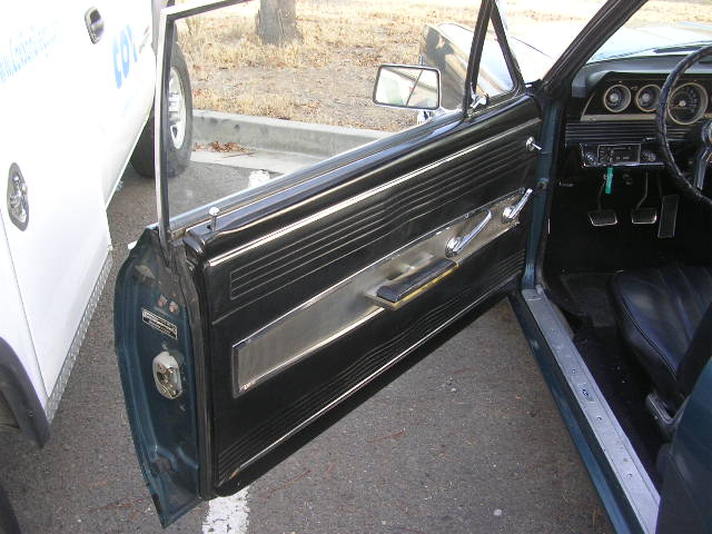 1966 Ford Falcon interior showing door panel, dashboard, steering wheel, and pedals. A white truck is partially visible outside
