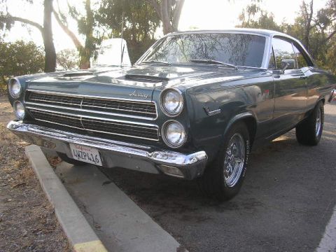 1975 Ford Ranchero - A green Mercury Comet is parked on the side of the road, showing its front grille and headlights.
