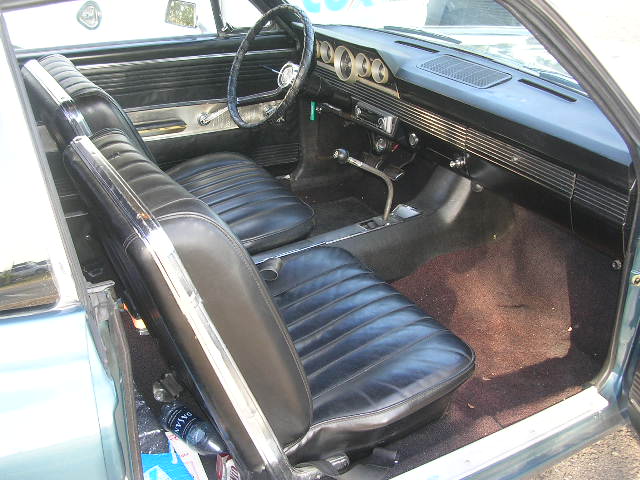 Light blue car interior with black vinyl seats, dashboard with horizontal vents, and floor shifter