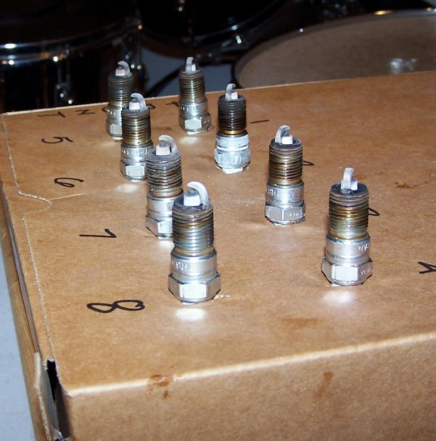 Eight spark plugs arranged on a cardboard box with numbers 1-8 written on it