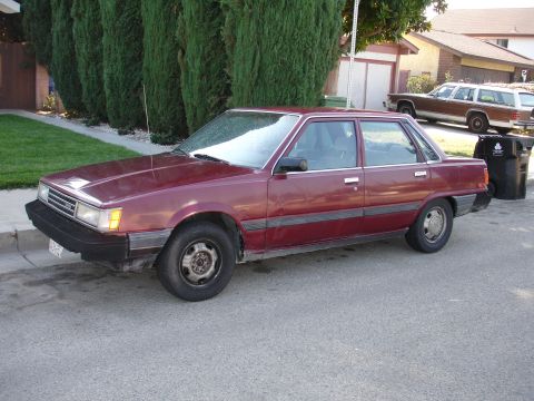 1993 Ford Taurus - A maroon sedan is parked on the street, with a wood-paneled station wagon visible in the background.