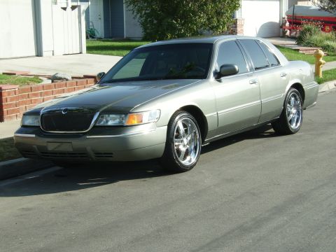2000 Mercury Grand Marquis - A silver Mercury Grand Marquis with custom chrome wheels is parked on a residential street.