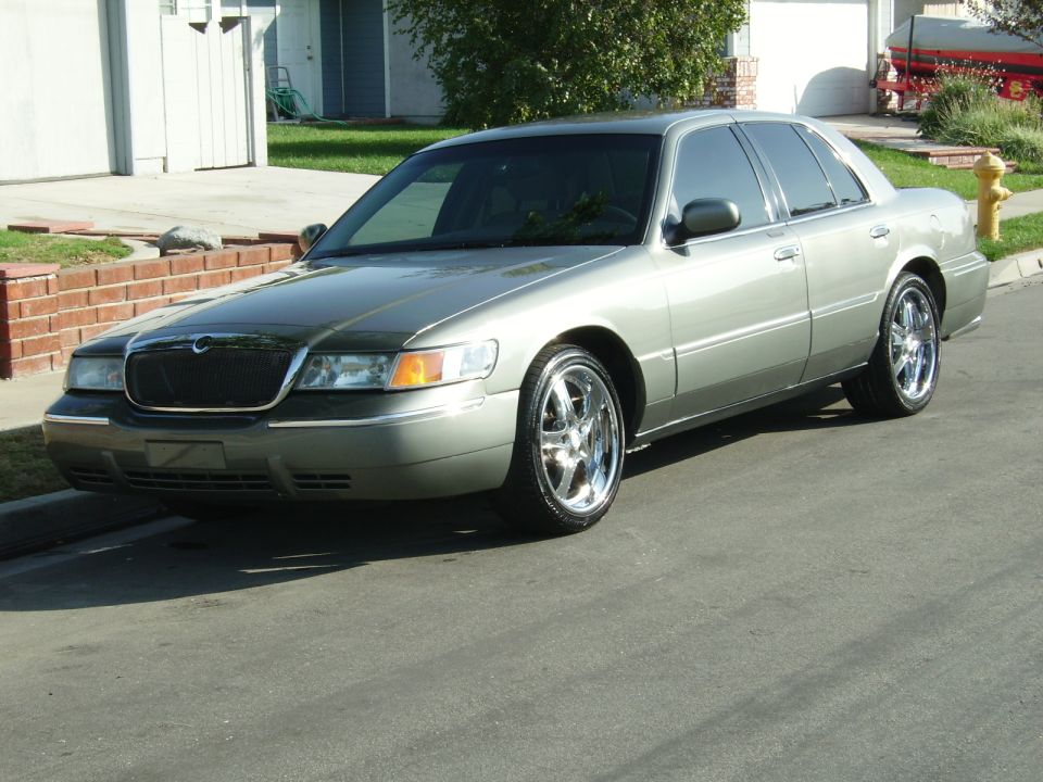 Silver Mercury Grand Marquis parked on a street. Chrome wheels and tinted windows