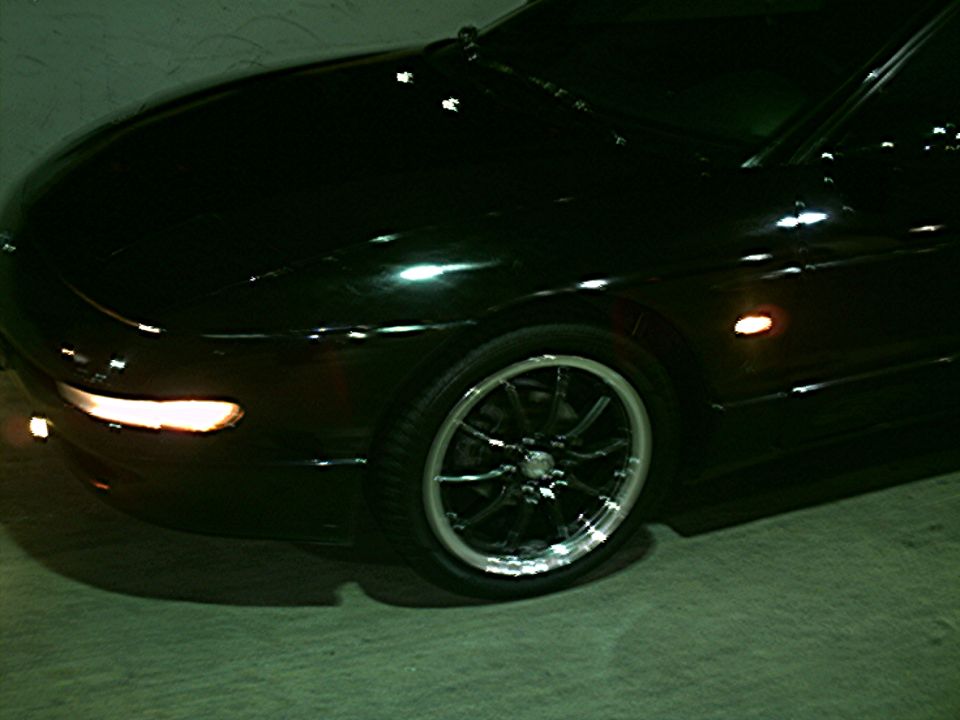 Black car front corner with aftermarket wheels and illuminated headlight