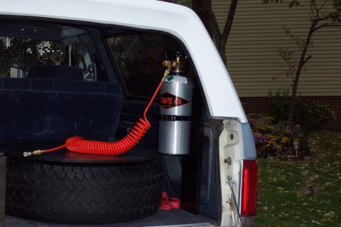 1987 Ford Bronco - An air compressor tank and coiled hose are mounted inside the cargo area of a vehicle, resting on a spare tire.