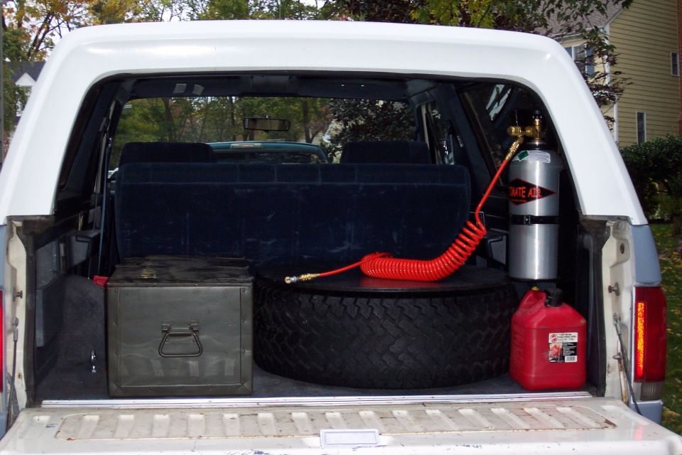 White SUV cargo area with spare tire, toolbox, red gas can, and CO2 tank